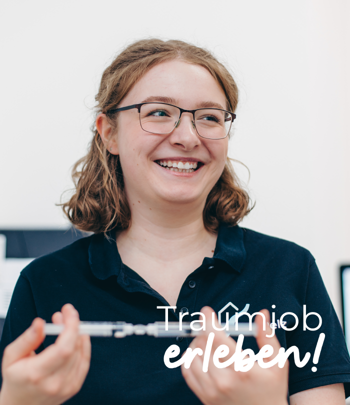 Eine junge lächelnde, braunhaarige Frau mit Brille blickt eine unbekannte Person an. Der Schriftzug "Traumjob erleben!" ist auf das Bild gesetzt.