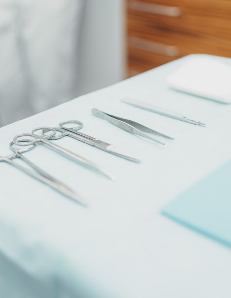Auf einer weißen Oberfläche sind verschiedene Instrumente, wie Scheren und Pinzetten zu sehen, die fein säuberlich aneinandergereiht sind.