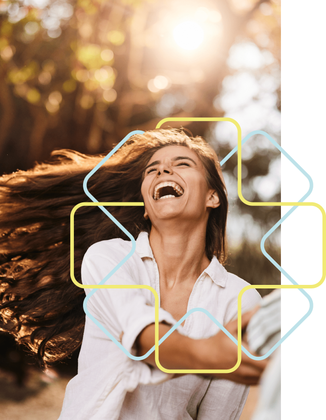 Eine Frau wirft sich lachend zurück, ihr langes braunes Haar weht im Wind hinter ihr. Der sonnige Wald im Hintergrund ist verschwommen. Sie trägt eine weiße Bluse und greift nach vorne. Das geometrische Stilelement der Praxis umrahmt ihr Gesicht.