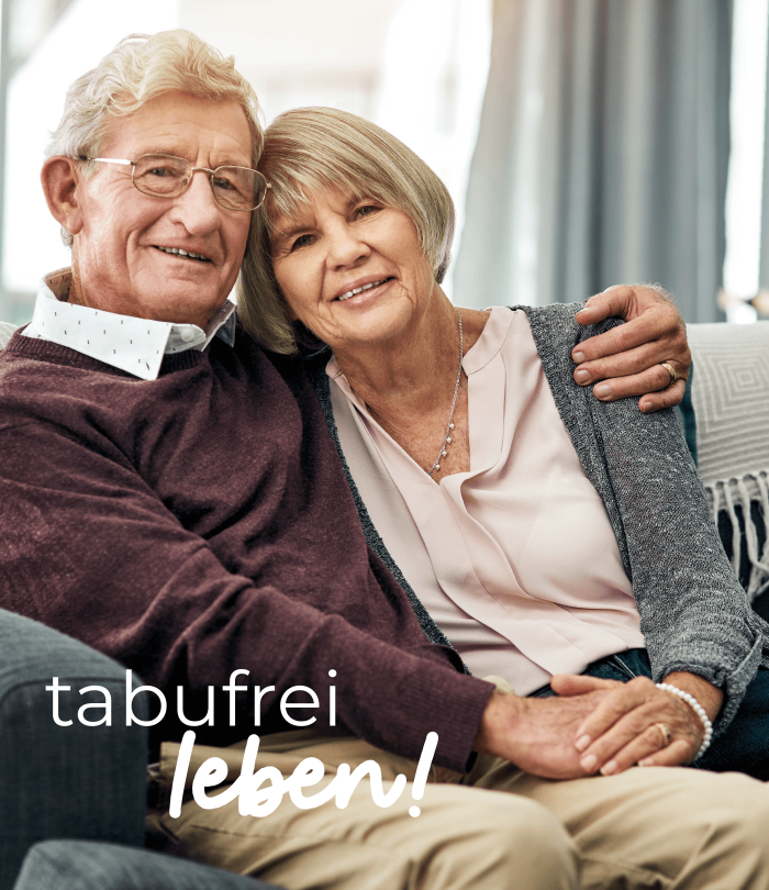 Ein älteres Ehepaar sitzt auf einem Sofa. Der Mann hat den Arm um seine Frau gelegt. Sie halten sich an den Händen und lächeln in die Kamera. Er trägt Hemd und Pullover, sie eine Bluse mit Jäckchen.Auf dem Bild steht "tabufrei leben!".