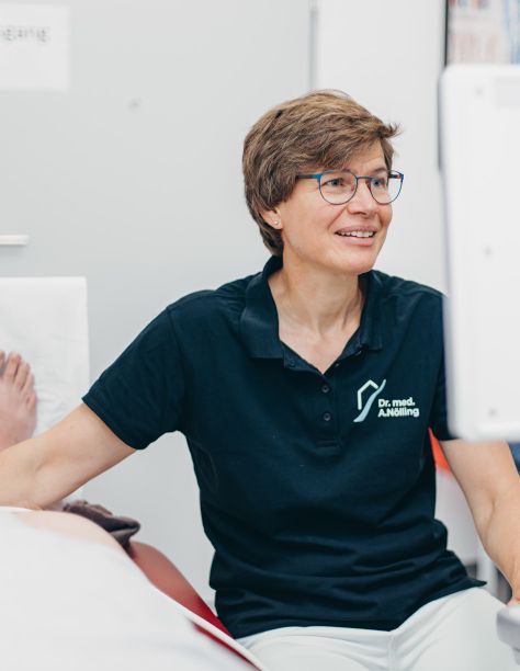 Foto von Dr. med. Anke Nölling, die konzentriert auf einen Bildschirm blickt. Sie trägt das dunkelblaue Praxis-Shirt der Praxisklinik am Flüsschen.