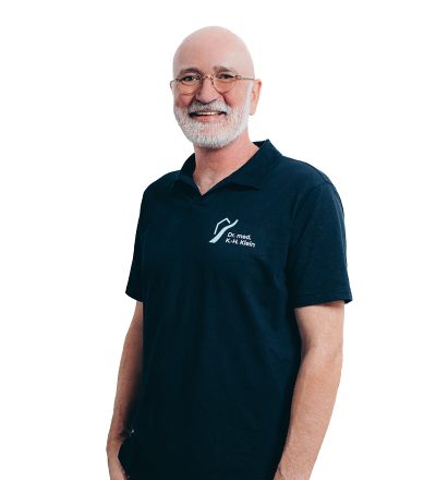 Portraitfoto von Dr. med. Karl-Hermann Klein, er trägt das Praxis-Shirt der Praxisklinik am Flüsschen, er ist Facharzt für Chirurgie, Phlebologie, Chirotherapie/manuelle Therapie