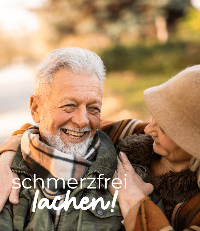 Älteres Paar lacht gemeinsam im Freien an einem sonnigen Herbsttag. Der Mann trägt eine grüne Jacke und einen karierten Schal, die Frau einen beigen Hut und eine Jacke mit Fellkragen. Beide schauen sich herzlich an. Im Bild steht der Schriftzug „schmerzfr